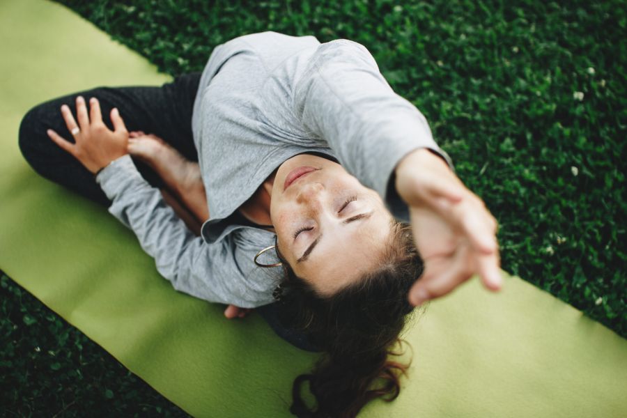 Woman is practicing yoga on a green lawn. Young woman relaxes in yoga pose outdoors